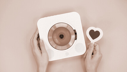 Hands holding white cd player and heart shape gift card on brown background. Colour of the year Mocha Mousse. Love music, Valentine day, Greeting,