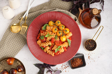 Plate of delicious fusilli pasta with tomatoes and basil on white background