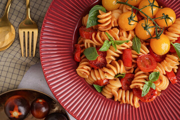 Plate of delicious fusilli pasta with tomatoes and basil on white background, closeup
