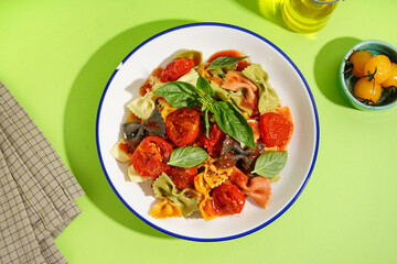 Bowl of delicious farfalle pasta with tomato and basil on green background