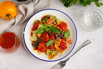 Bowl of delicious farfalle pasta with tomato and basil on white background
