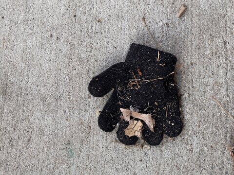 Small black wool glove lost on sidewalk with debris 