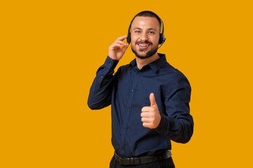 Male technical support agent in headset showing thumb-up on yellow background