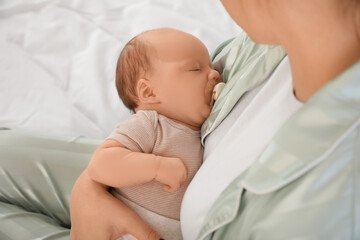 Mother holding her cute little sleeping baby on bed at home, closeup