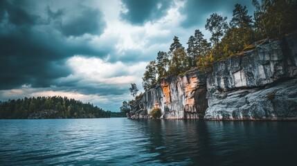 Fototapeta premium Dramatic lake view with cliff, trees, and stormy sky.