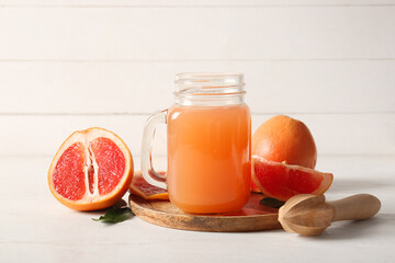 Mason jar with tasty grapefruit juice and fresh fruits on light wooden table