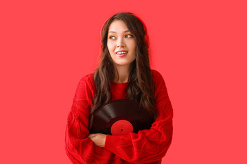 Beautiful young Asian woman in stylish sweater and modern headphones with vinyl disk on red background