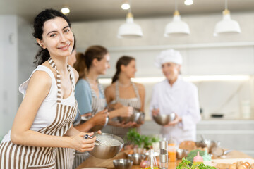 Young woman in apron learning to cook at cooking master class