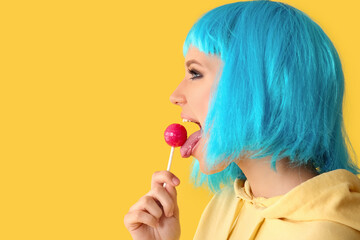 Beautiful young woman in blue wig with sweet lollipop on yellow background