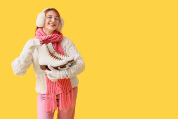 Beautiful young happy woman with ice skates on yellow background