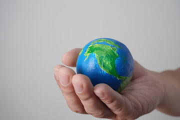 Hand holding green blue earth globe made of painted ball, over grey