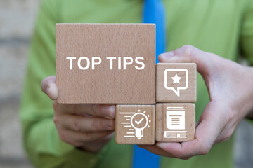 Concept of top tips. Business man holding wooden blocks with icons sees inscription: TOP TIPS.