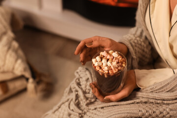 Beautiful young woman with cup of hot chocolate and marshmallows in evening at home, closeup