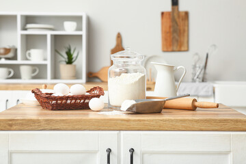 Flour in jar with rolling pin, scoop and eggs for preparing dough on kitchen counter