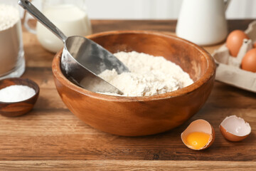 Bowl of flour with scoop and cracked egg for preparing dough on kitchen counter