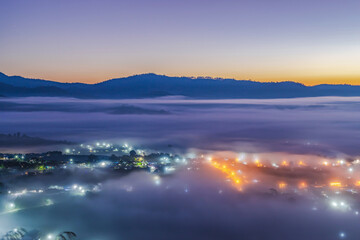 Fototapeta premium Mountain village in fog at beautiful sunset in spring with street lights. Foggy town at twilight. Travel