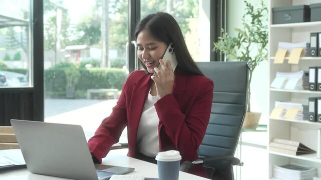A young Asian woman works diligently at her desk in a bright office room during the day. Surrounded by files, charts, and devices, she strategies on marketing funnels and SEO optimization.