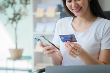 A young Asian woman works at her desk in an office room during the day. Surrounded by financial charts, files, and devices, she consults on credit reports, calculations, and credit risk assessments.
