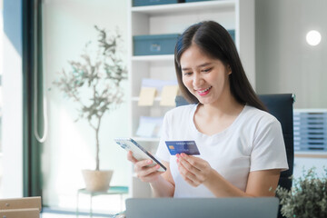 A young Asian woman works at her desk in an office room during the day. Surrounded by financial charts, files, and devices, she consults on credit reports, calculations, and credit risk assessments.