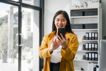 A young Asian woman works at her desk in an office, surrounded by paper files, financial charts, and devices. She focuses on HR, legal consulting, and compliance while managing time effectively.