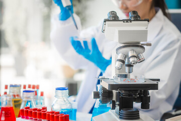 A young Asian woman works in a laboratory, conducting chemical and blood tests. Wearing goggles,...