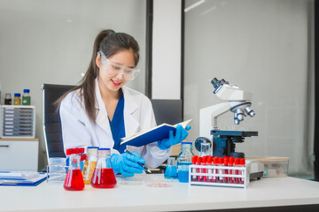 A young Asian woman works in a laboratory, conducting chemical and blood tests. Wearing goggles,...