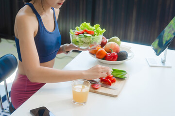 A young Asian housewife enjoys a healthy lifestyle at home, balancing fitness routines with relaxation. She sits on a modern sofa, eating a fresh salad and fruit while embracing healthy habits.