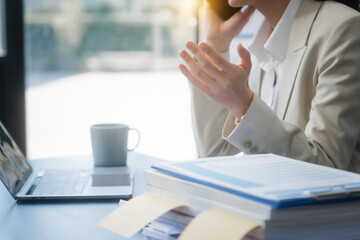 A young Asian businesswoman works alone at a desk with a laptop, stack of papers, and documents....