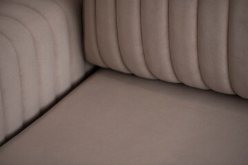 Soft beige velour sofa quilted with straight lines of stitching. Part of the sofa with armrest and pillows close-up with copy space.