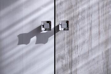 Close-up of cabinet doors with textured striped pattern and silver square handles in shadows and sunlight. Combined two-tone furniture doors.