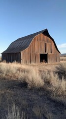 Obraz premium A rustic wooden barn stands in a grassy landscape under a clear sky.