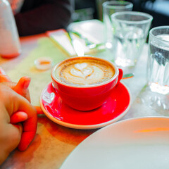 Romantic Coffee Date With Latte Art in a Cozy Cafe Setting Featuring a Red Coffee Cup and Holding Hands for a Perfect Morning Experience