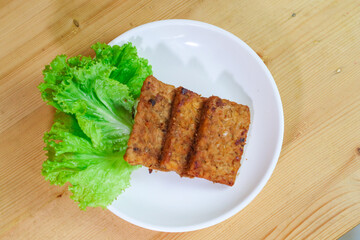 Indonesian traditional food named tempe bacem i.e. tempeh cooked with coconut sugar and spices prior frying