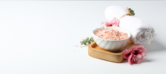 Sea salt in bowl, towel and flowers on gray background, space for text