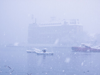Snowy Istanbul harbor view with boats and a historic building in soft snowfall