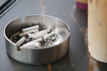 An ashtray containing cigarettes situated next to a refreshing beverage