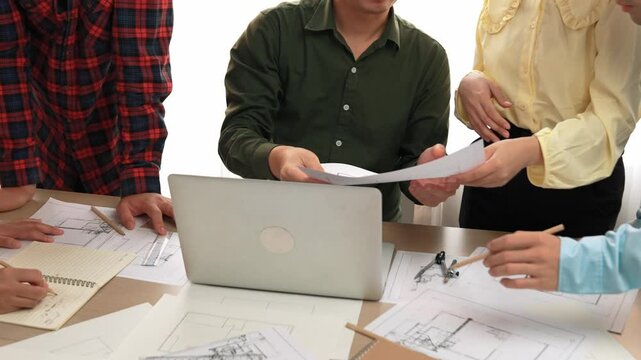 Smart architect and safety engineer discussion about building plan on table with architectural document, measurement tools and wooden block scatter around at modern office. Closeup. Delineation.