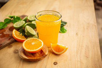 Orange juice in a glass surrounded by orange slices, lime and lime leaves on a wooden table