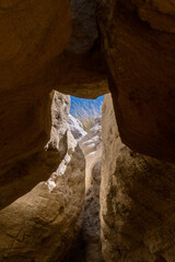 Natural rock formation with a narrow opening revealing clear blue sky in a canyon in the desert during daylight, showcasing the beauty of geological features in the landscape
