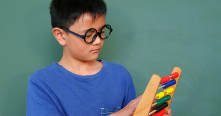 Front view of Asian schoolboy solving math problem with abacus in a classroom at school