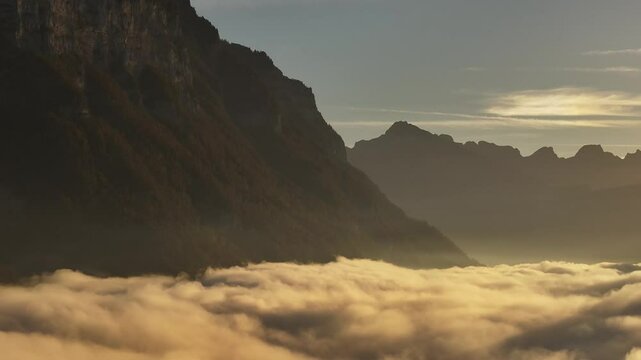 Drone flight over the Swiss Alps during a stunning sunrise, abobe the clouds.