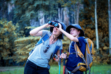 Naklejka premium Hikers or explorers on journey carrying backpack, trekking poles and holding binoculars looks into the distance observing and possibly guide trekking and trail exploration holiday ecotourism concept.