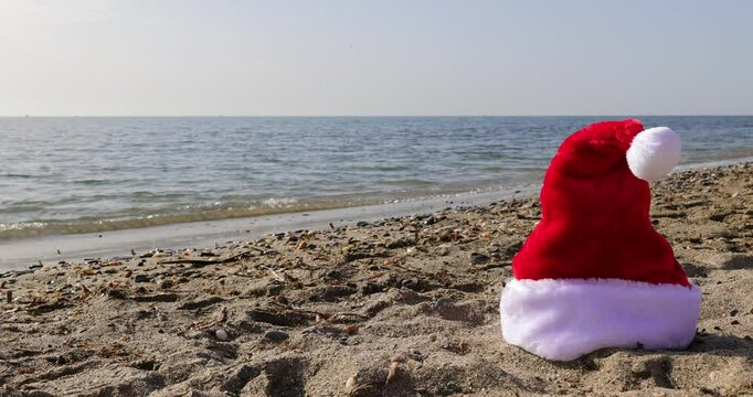 Footage on the beach of Sitio de Calahonda in Spain showing a Christmas festive Santa hat on the sand by the ocean indicating a Christmas by the sea concept