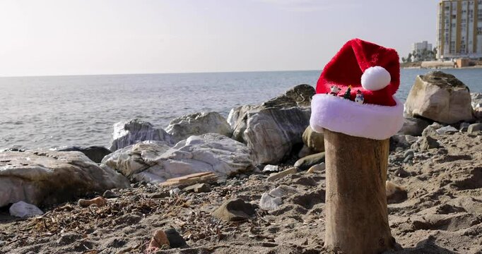 Footage on the beach of Sitio de Calahonda in Spain showing a Christmas festive Santa hat on the sand by the ocean indicating a Christmas by the sea concept