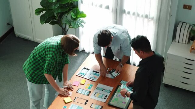 Top view of smart Ui designer brainstorming and planning about Ux Uo design or mobile interface wireframe design with diverse develop team. Caucasian programer walking and joining meeting.Convocation.