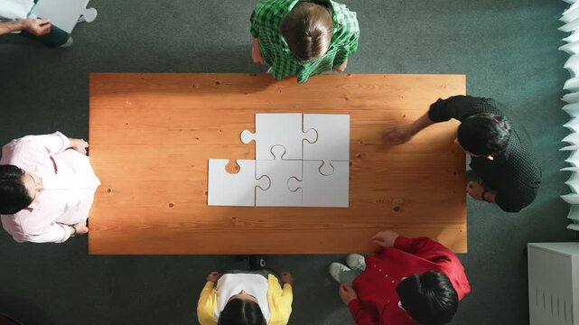 Top view of business man gathering last piece of jigsaw to complete puzzle. Group of diverse team working together to solve the puzzle while putting hands together and clapping hands. Convocation.