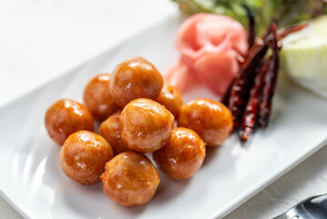 A plate of savory meatball appetizers with pickled ginger and chili peppers.