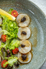 Close-up of a plate of thinly sliced fish with a side salad and lemon wedge.