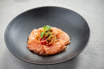 Close-up of a delicious salmon salad with fresh herbs and vegetables on a black plate.