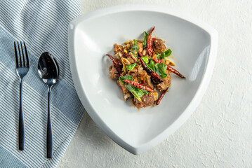 A plate of stir-fried meat and vegetables with a side of fork and spoon